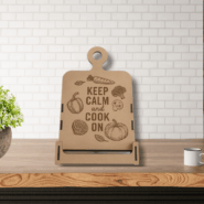 Wooden kitchen sign standing on a rustic wood surface against a white brick wall, flanked by potted green plants.
