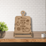 Engraved wooden Keep Calm and Cook On stand on a white marble kitchen counter next to cooking utensils and window light.