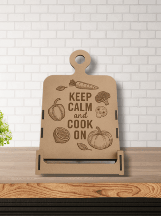 Engraved wooden Keep Calm and Cook On stand on a white marble kitchen counter next to cooking utensils and window light.
